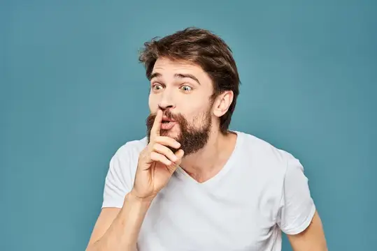 Бородатый мужчина прикладывает палец к губам на синем фоне