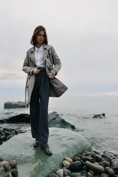 Молодая женщина в плаще стоит на камне у моря