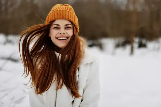 Улыбающаяся девушка в оранжевой шапке на зимней прогулке