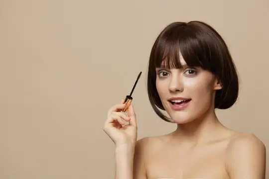 Молодая женщина с тушью для ресниц на бежевом фоне
