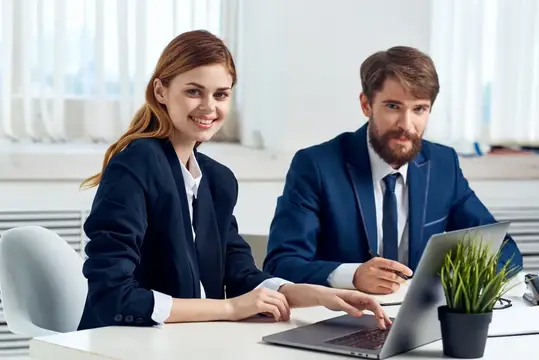 Улыбающиеся мужчина и женщина в офисных костюмах работают за ноутбуком