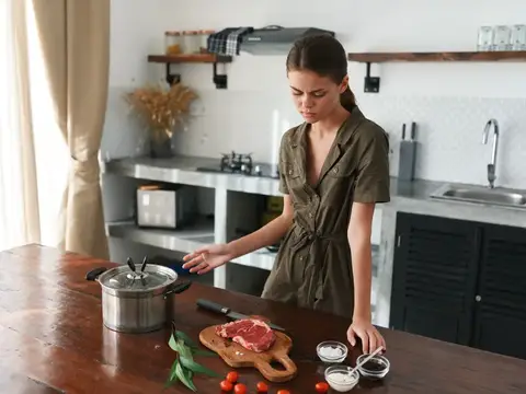 Молодая женщина готовит мясо на кухне у деревянного стола
