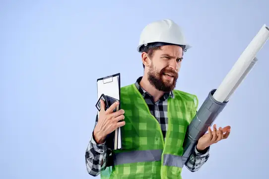 Бородатый мужчина в каске и жилете держит чертежи и планшет