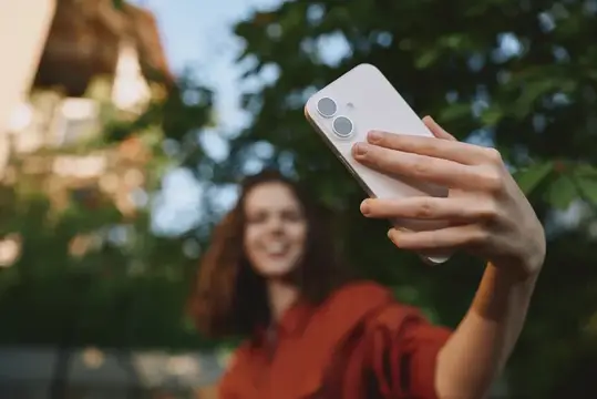 Улыбающаяся девушка делает селфи на смартфон на улице