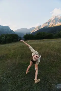 Молодая женщина танцует на лугу на фоне гор в тёплом вечернем свете