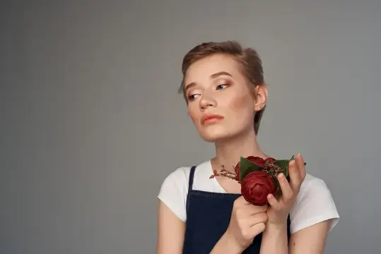 Молодая женщина с короткой стрижкой держит красную розу на сером фоне