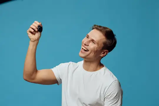 Улыбающийся мужчина в белой футболке держит брелок на синем фоне