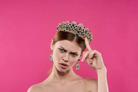 Задумчивая девушка в короне с изумрудами на розовом фоне
