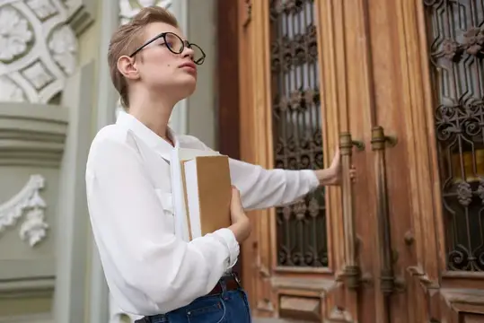 Студентка в очках с книгой у старинной деревянной двери
