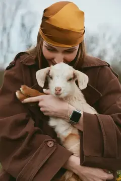 Искренний момент нежной связи между человеком и козленком на природе, подчеркивающий сострадание, ответственность и повседневный фермерский образ жизни
