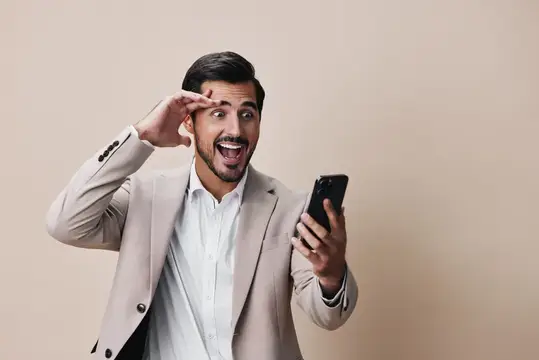 Молодой мужчина в костюме с улыбкой держит смартфон, показывая сообщение на экране