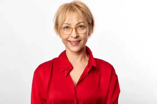 Улыбающийся портрет пожилой женщины в студии, в красной блузке и очках, нейтральный белый фон, расслабленная поза голова-плечи, дружелюбные глаза, мягкое ровное освещение, свободное пространство