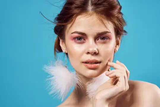 Молодая женщина с розовым макияжем и пушистыми серьгами на бирюзовом фоне