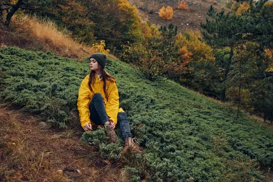 Девушка в жёлтой куртке сидит на склоне горы осенью