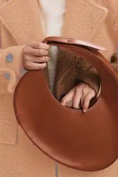 Женщина в бежевом пальто держит круглую коричневую сумку