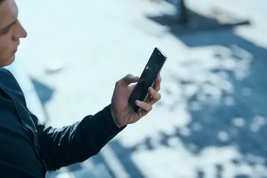 Мужчина в профиль смотрит в смартфон на фоне зимней улицы