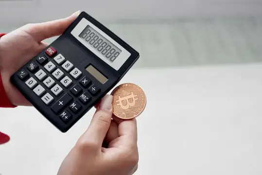 Руки держат калькулятор и золотую монету биткоин