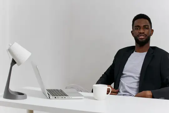 Сосредоточенный мужчина работает за письменным столом на своем ноутбуке, рядом стоит чашка кофе, обстановка уютного домашнего офиса