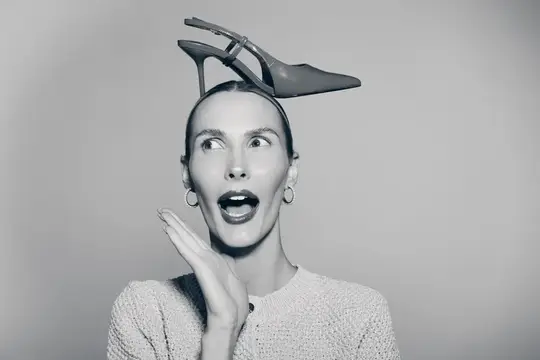 Удивлённая женщина с туфлей на голове на сером фоне