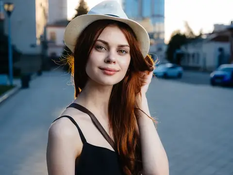 Модель с рыжими волосами на улице в городе, одетая в чёрное платье и белую шляпу