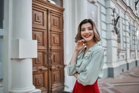 Улыбающаяся брюнетка в светлой блузе на фоне старинного здания