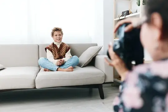 Кудрявый мальчик позирует фотографу на диване