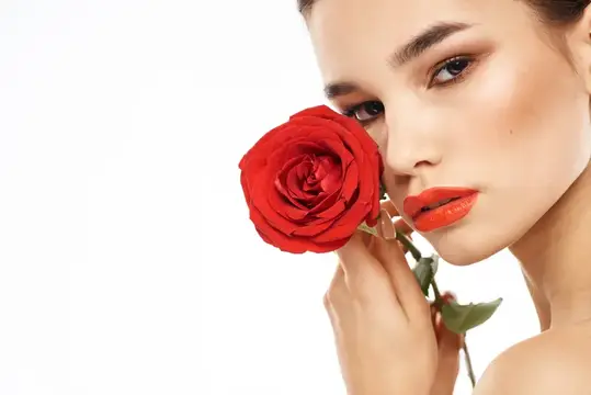 Молодая женщина с красной розой у лица на белом фоне