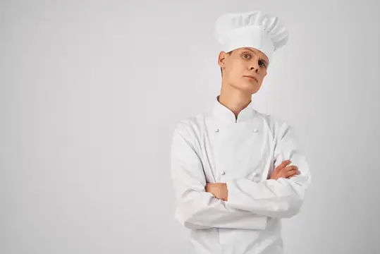 Молодой повар в белом колпаке и кителе со скрещёнными руками