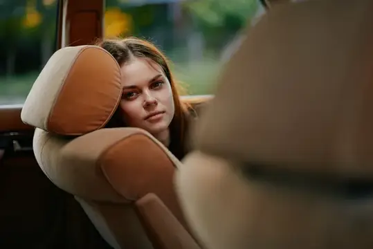 Безмятежная молодая женщина сидит в автомобиле, опираясь на мягкое сиденье, погруженная в раздумья