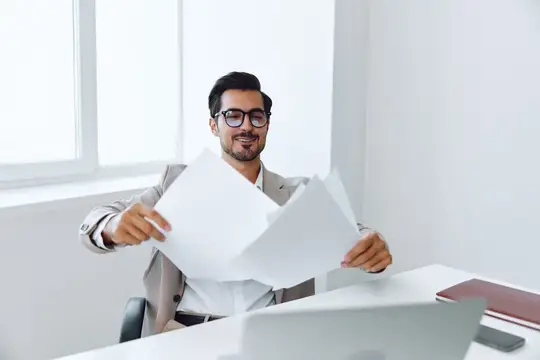 Улыбающийся бородатый мужчина в очках разбирает бумаги в офисе