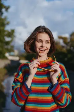 Улыбающаяся девушка с дужкой очков в зубах на фоне неба