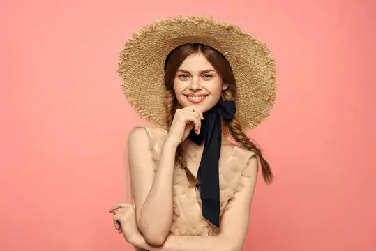 Улыбающаяся девушка в соломенной шляпе с чёрной лентой на розовом фоне