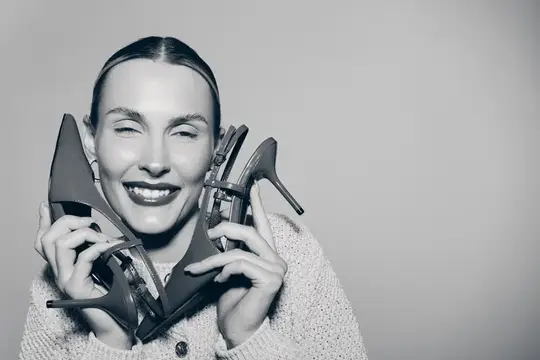 Улыбающаяся женщина с закрытыми глазами держит туфли у лица