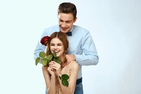 Улыбающийся парень обнимает девушку с красной розой