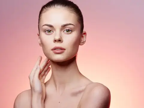 Молодая женщина с гладкой кожей на розовом фоне касается щеки