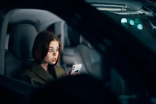Испуганная девушка со смартфоном в салоне автомобиля ночью