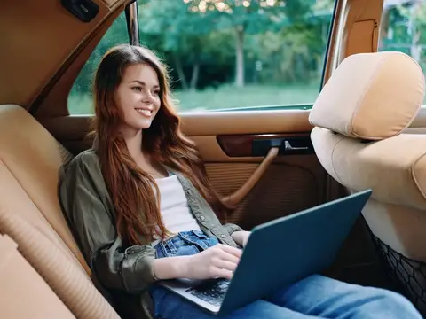 Улыбающаяся девушка с ноутбуком на заднем сиденье автомобиля