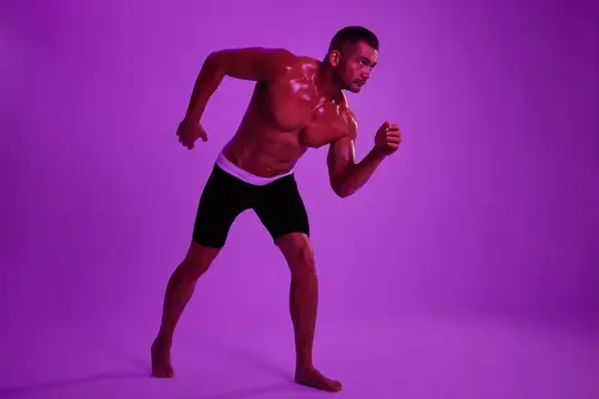 Спортивный мужчина, культурист в трусах с обнаженным торсом и прессом, изображен в полный рост на фоне фиолетового цветного света