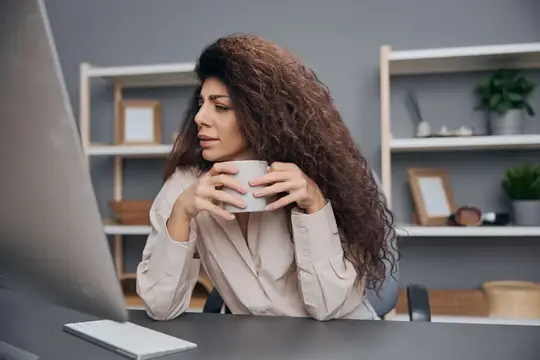 Кудрявая женщина с кружкой смотрит на монитор в офисе