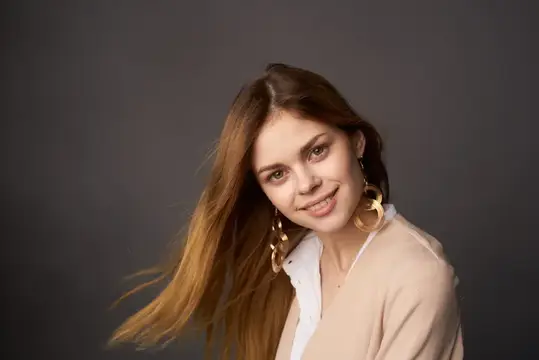 Молодая шатенка с золотыми серьгами улыбается на тёмном фоне
