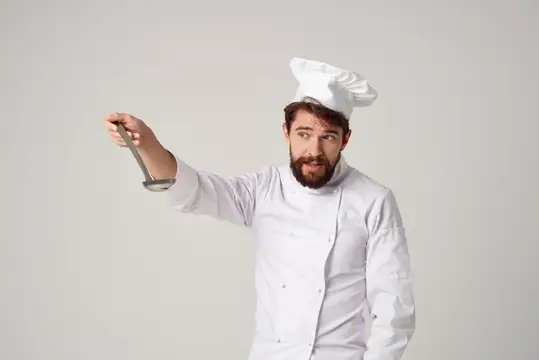 Повар с половником в руке готовит еду на профессиональной кухне ресторана