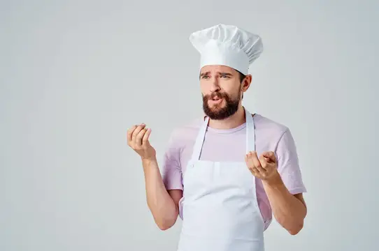 Бородатый мужчина в поварском колпаке и фартуке жестикулирует