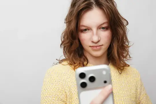 Молодая девушка смотрит в смартфон на светлом фоне