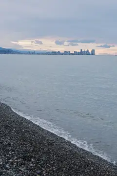 Галечный берег и силуэт города вдали под пасмурным небом