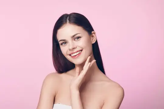 Красивая молодая женщина с чистой кожей улыбается и позирует на розовом фоне