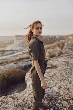 Молодая женщина в комбинезоне стоит на каменистом плато