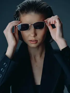Девушка в чёрном пиджаке поправляет солнцезащитные очки