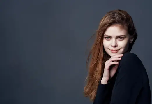 Молодая рыжеволосая женщина с лёгкой улыбкой на тёмном фоне