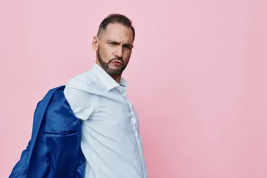 Мужчина с бородой в белой рубашке с пиджаком на плече на розовом фоне