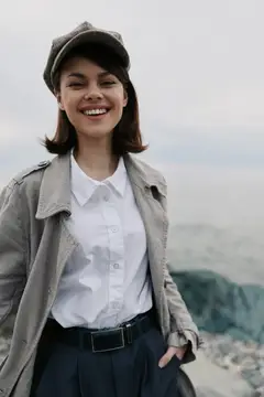 Улыбающаяся девушка в кепке и плаще на фоне гор